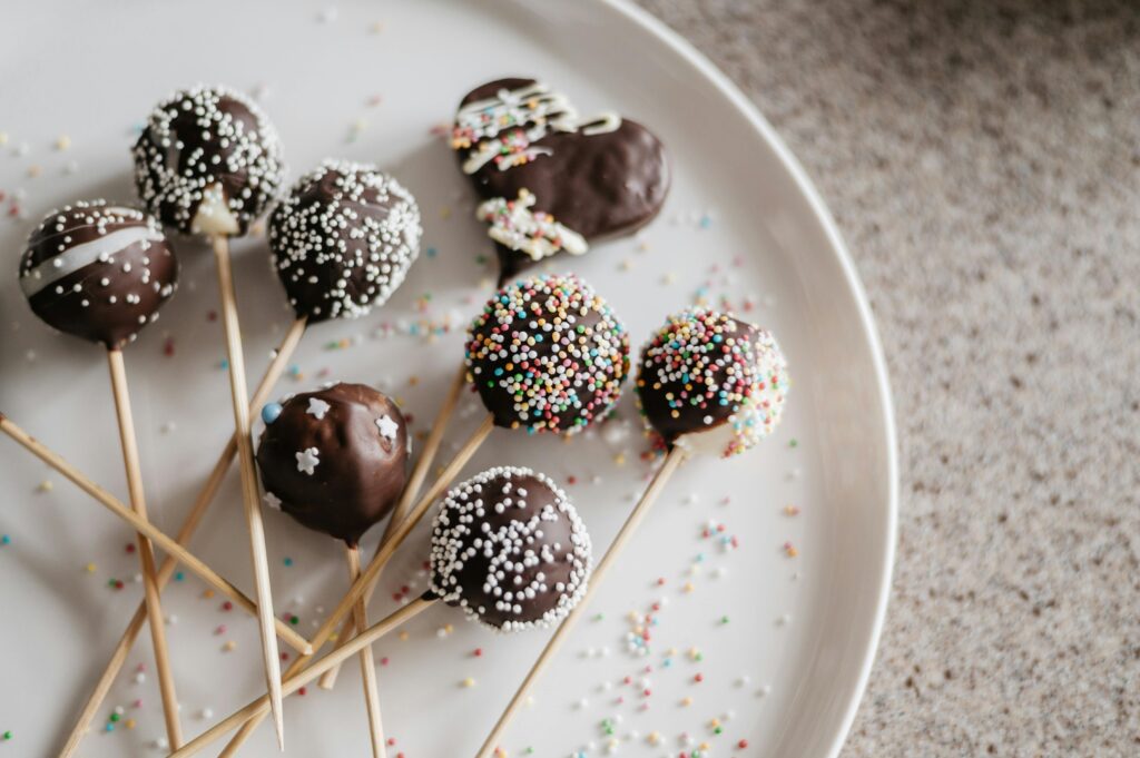 Close-up of chocolate cake pops with colorful sprinkles on a plate.