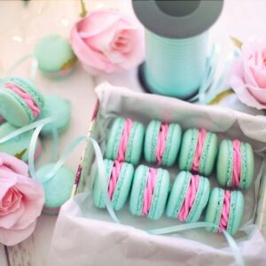 A delightful display of pastel macarons with pink roses and teal ribbons.