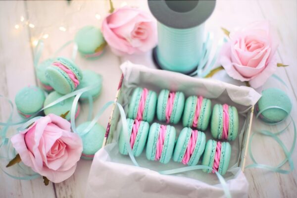 A delightful display of pastel macarons with pink roses and teal ribbons.