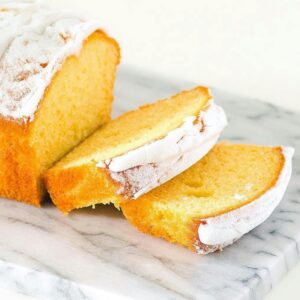 Delicious sliced pound cake with sugar icing on a marble surface, perfect for dessert lovers.