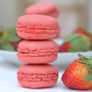 Close-up of pink macarons stacked with fresh strawberries in a soft focus setting.