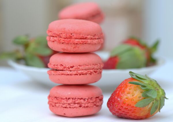 Close-up of pink macarons stacked with fresh strawberries in a soft focus setting.